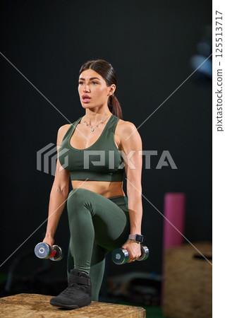 woman engages in strength training routine lifting dumbbells while balancing on one leg in fitness studio. workout focuses on building strength and stability. woman engages in strength training routine lifting dumbbells while balancing on one leg in fitness studio. workout focuses on building strength and stability. 125513717