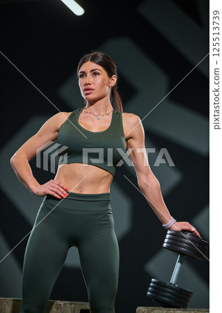confident woman stands dumbbell in contemporary fitness center. She showcases her strength and dedication fitness in dynamic environment. confident woman stands dumbbell in contemporary fitness center. She showcases her strength and dedication fitness in dynamic environment. 125513739
