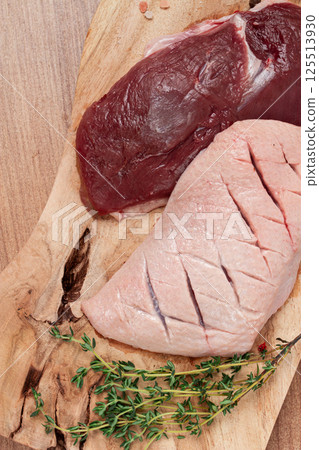 Fresh raw duck breasts, on a wooden chopping board, with herbs and spices, no people 125513930