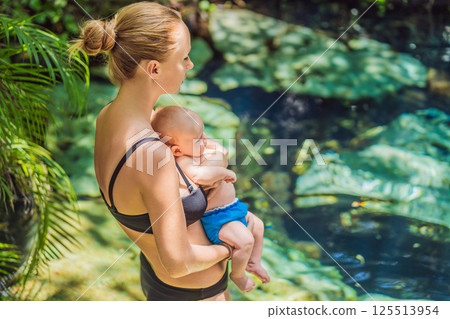 Mother with her baby standing by a Mexican cenote with turquoise water. Family adventure, travel, and nature bonding concept 125513954