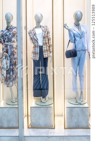 Female mannequins in elegant clothing are displayed in a store window 125513989