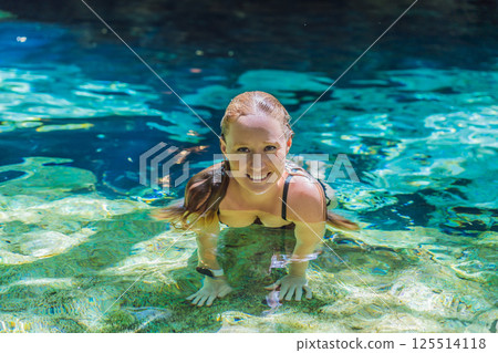 Female tourist enjoying a refreshing swim in a Mexican cenote with turquoise water. Adventure, travel, and nature exploration concept 125514118