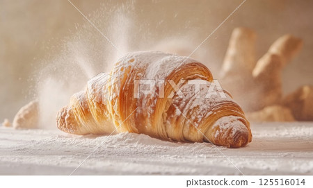 A golden croissant rests on a wooden table, dusted with flour. The warm kitchen atmosphere emphasizes the freshness of the pastry, inviting indulgence and comfort 125516014