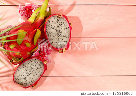 Dragon fruit, pitaya on a sunny table with shadows from a palm tree and orchid flowers, advertising card for a store. Summer banner with tropical exotic fruits. Healthy vegan food for weight loss 125516063