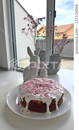 Deliciously decorated Easter cake with icing and pink sprinkles, surrounded by charming bunnies Deliciously decorated Easter cake with icing and pink sprinkles, surrounded by charming bunnies 125516066