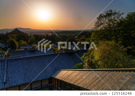 Sunset sky at Todaiji Temple's Nigatsudo Hall. The sun sets over the Ikoma mountain range, painting the sky and temple grounds golden. 125516246