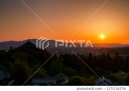 Sunset sky at Todaiji Temple's Nigatsudo Hall. The sun sets over the Ikoma mountain range, painting the sky and temple grounds golden. 125516256