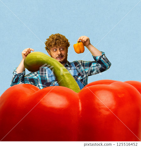 Farmer man compares giant red pepper and small yellow pepper against blue background 125516452