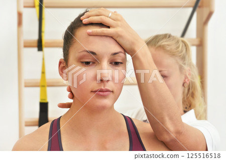 Young physiotherapist exercising with her female patient, fixing head and neck using hand, during exercise Young physiotherapist exercising with her female patient, fixing head and neck using hand, during exercise 125516518