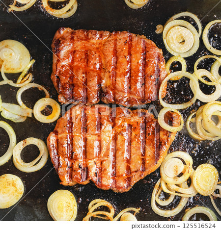 Two pork cutlets steaks and onion cut to slices, grilled on electric grill, overhead view 125516524