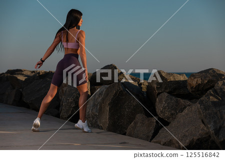 woman is exercising stretching water's edge sunset. glowing sky and tranquil sea create peaceful atmosphere for her wellness routine. 125516842