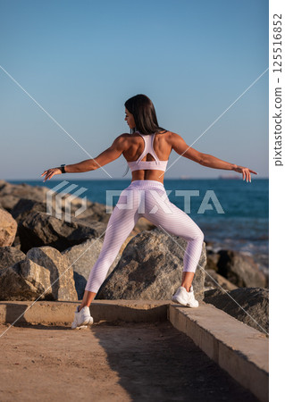 person focusing on fitness practices is seen exercising on coastal path surrounded rocks. sun sets in background creating serene atmosphere. person focusing on fitness practices is seen exercising on coastal path surrounded rocks. sun sets in background creating serene atmosphere. 125516852