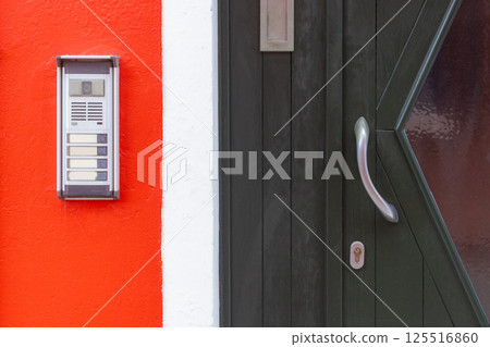 Door intercom on red wall in Burano Italy 125516860