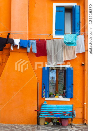 Colorful orange wall with blue shutters and laundry in Burano Italy 125516870