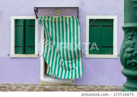 Purple house facade with green shutters and striped curtain in Burano Italy Purple house facade with green shutters and striped curtain in Burano Italy 125516875