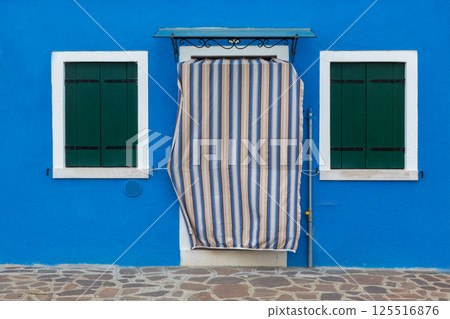 Blue house facade with green shutters and striped curtain Burano Italy Blue house facade with green shutters and striped curtain Burano Italy 125516876