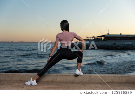 person performs stretching routine water enjoying stunning sunset. Waves crash gently while sky is painted warm colors creating peaceful atmosphere. 125516889