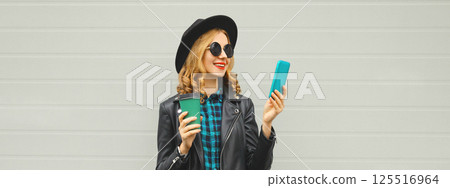 Stylish happy smiling modern young woman with phone, girl holding smartphone in black hat, jacket 125516964