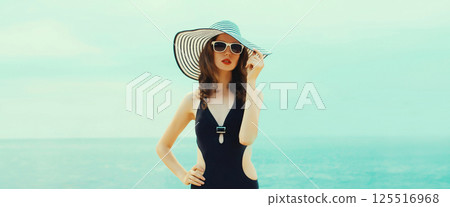 Summer beautiful young woman in bikini swimsuit, black hat, stylish girl posing on the beach on sea 125516968