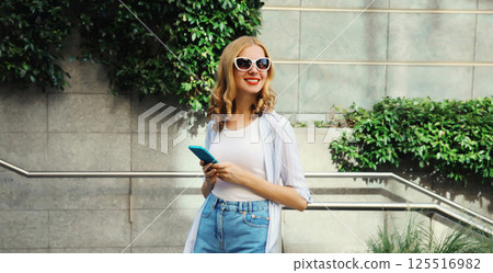 Stylish modern happy smiling young woman with phone in city park, girl holding smartphone on street 125516982