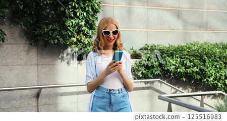 Stylish modern happy smiling young woman with phone in city park, girl holding smartphone on street Stylish modern happy smiling young woman with phone in city park, girl holding smartphone on street 125516983