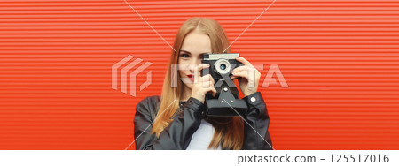 Portrait of stylish young woman photographer with film camera, modern girl taking a picture on red 125517016