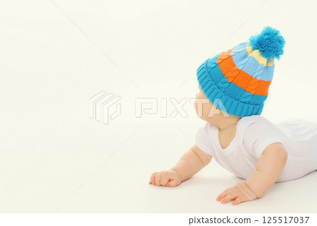Happy baby in winter knitted hat crawling on the floor playing on white studio background Happy baby in winter knitted hat crawling on the floor playing on white studio background 125517037