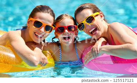 Three joyful friends wearing colorful sunglasses laugh together in a sparkling blue pool surrounded by inflatable rings embodying the excitement of a perfect summer day. Three joyful friends wearing colorful sunglasses laugh together in a sparkling blue pool surrounded by inflatable rings embodying the excitement of a perfect summer day. 125517121
