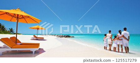 A joyful family enjoys time together on a pristine beach under clear blue skies. Bright orange umbrellas provide shade as they cherish moments by the shimmering water. 125517279