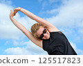 Woman stretching arms overhead outdoors under bright sky, enjoying fitness and wellness routine, focusing on flexibility, strength, and energy in a natural environment 125517823