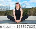 Woman practicing yoga outdoors, sitting in butterfly pose on a mat, enjoying fresh air, natural surroundings, and blue sky, embracing mindfulness and relaxation. 125517825