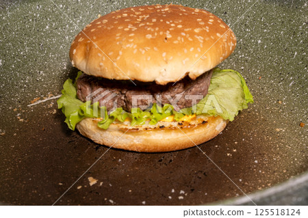 A fresh sesame seed hamburger bun with beef patty, lettuce, and sauce rests on a griddle, showcasing a classic burger ready to enjoy. A fresh sesame seed hamburger bun with beef patty, lettuce, and sauce rests on a griddle, showcasing a classic burger ready to enjoy. 125518124