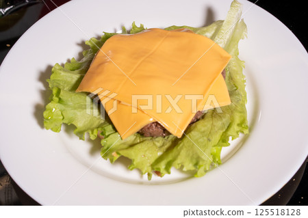 A lettuce-wrapped burger with a beef patty and melted yellow cheese on a white plate. A perfect low-carb, keto-friendly meal option. 125518128