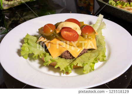 An open-faced cheeseburger on a white plate with lettuce, tomato, pickles, and mayonnaise. A bright, fresh take on a classic meal. 125518129