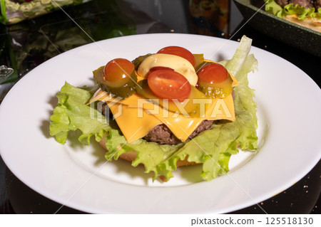 An open-faced cheeseburger on a white plate with lettuce, tomato, pickles, and mayonnaise. A bright, fresh take on a classic meal. 125518130