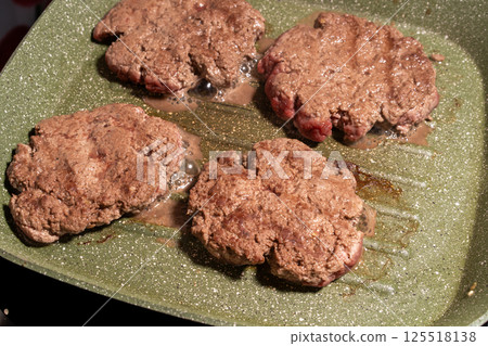 Four sizzling hamburger patties cook on a green griddle, showing texture, grease, and browning. A snapshot of burger preparation at its finest. 125518138