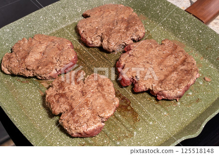 Four sizzling hamburger patties cook on a green griddle, showing texture, grease, and browning. A snapshot of burger preparation at its finest. 125518148