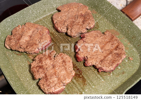 Four sizzling hamburger patties cook on a green griddle, showing texture, grease, and browning. A snapshot of burger preparation at its finest. 125518149