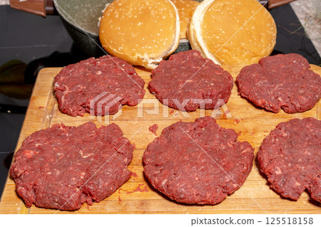 Fresh, raw hamburger patties on a wooden cutting board, ready for cooking. The texture and arrangement highlight the simplicity of burger preparation. Fresh, raw hamburger patties on a wooden cutting board, ready for cooking. The texture and arrangement highlight the simplicity of burger preparation. 125518158