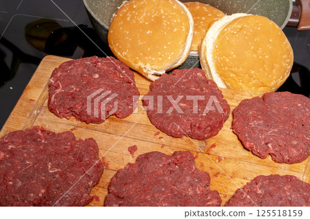 Fresh, raw hamburger patties on a wooden cutting board, ready for cooking. The texture and arrangement highlight the simplicity of burger preparation. 125518159