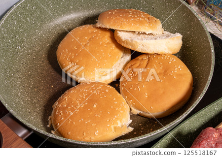Toasted sesame seed buns arranged in a frying pan, showcasing the preparation of fresh bread for burgers or sandwiches in a homey style. Toasted sesame seed buns arranged in a frying pan, showcasing the preparation of fresh bread for burgers or sandwiches in a homey style. 125518167