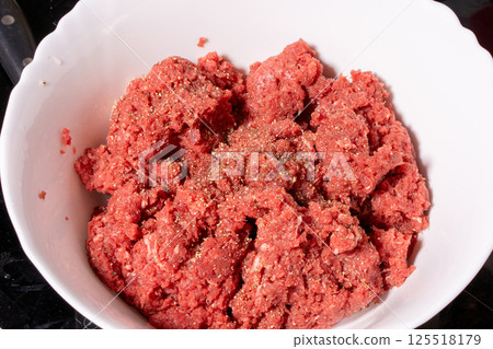 Seasoned raw ground meat in a scalloped white bowl with a coarse reddish texture. Ideal for making burgers, meatballs, or patties. 125518179