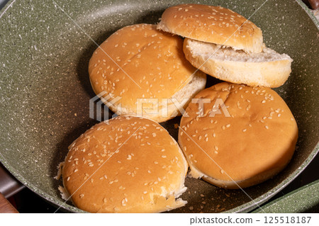 Toasted sesame seed buns arranged in a frying pan, showcasing the preparation of fresh bread for burgers or sandwiches in a homey style. 125518187