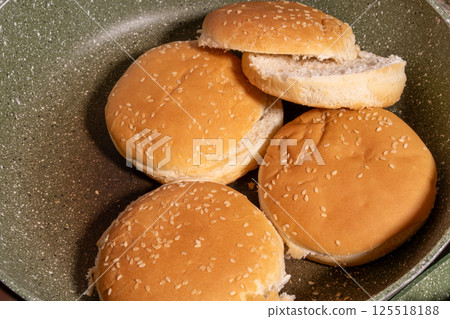 Toasted sesame seed buns arranged in a frying pan, showcasing the preparation of fresh bread for burgers or sandwiches in a homey style. Toasted sesame seed buns arranged in a frying pan, showcasing the preparation of fresh bread for burgers or sandwiches in a homey style. 125518188
