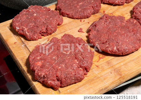 Fresh, raw hamburger patties on a wooden cutting board, ready for cooking. The texture and arrangement highlight the simplicity of burger preparation. Fresh, raw hamburger patties on a wooden cutting board, ready for cooking. The texture and arrangement highlight the simplicity of burger preparation. 125518191