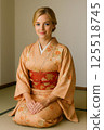 A blonde foreign woman sitting upright in a Japanese-style room wearing a kimono with a red obi 125518745