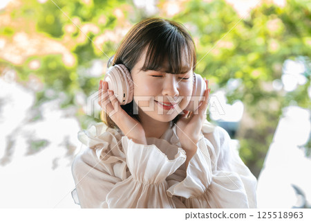 A young woman listening to music in a room with a view of fresh greenery 125518963