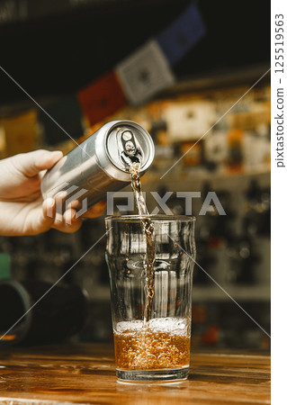 Pouring Cold Beer From an Aluminum Can Into Glass on Wooden Bar Counter 125519563