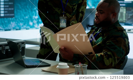 Angry army expert in a command post power base monitors satellite footage, yelling at soldier and throwing papers. Frustrated officer looks at real time data for operational success. Camera A. 125519803