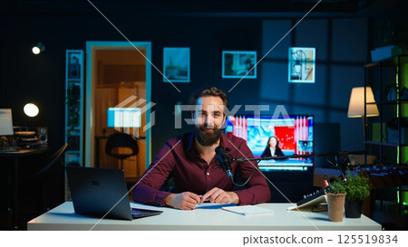 Happy influencer using microphone, arriving in dimly lit home studio interior, chatting with fans. Smiling man surrounded by podcast recording equipment in apartment starting stream, camera B Happy influencer using microphone, arriving in dimly lit home studio interior, chatting with fans. Smiling man surrounded by podcast recording equipment in apartment starting stream, camera B 125519834